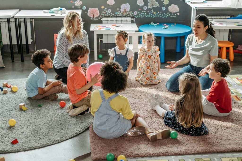 Diverse group of young children sitting in circle on carpet with two female teachers during interactive classroom learning session