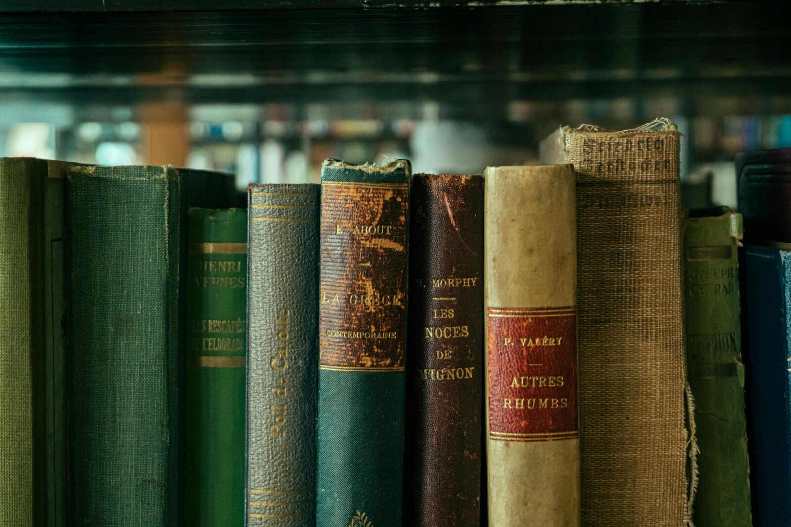 Row of vintage books with worn leather and cloth spines displaying titles and author names on library shelf