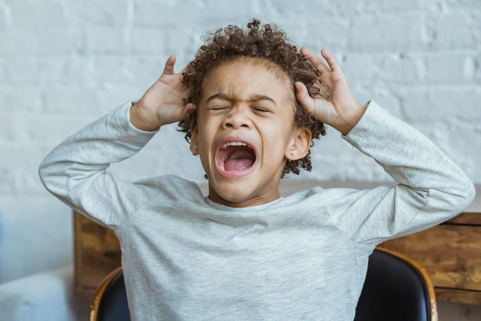 Young child with curly hair screaming with mouth open and hands covering ears