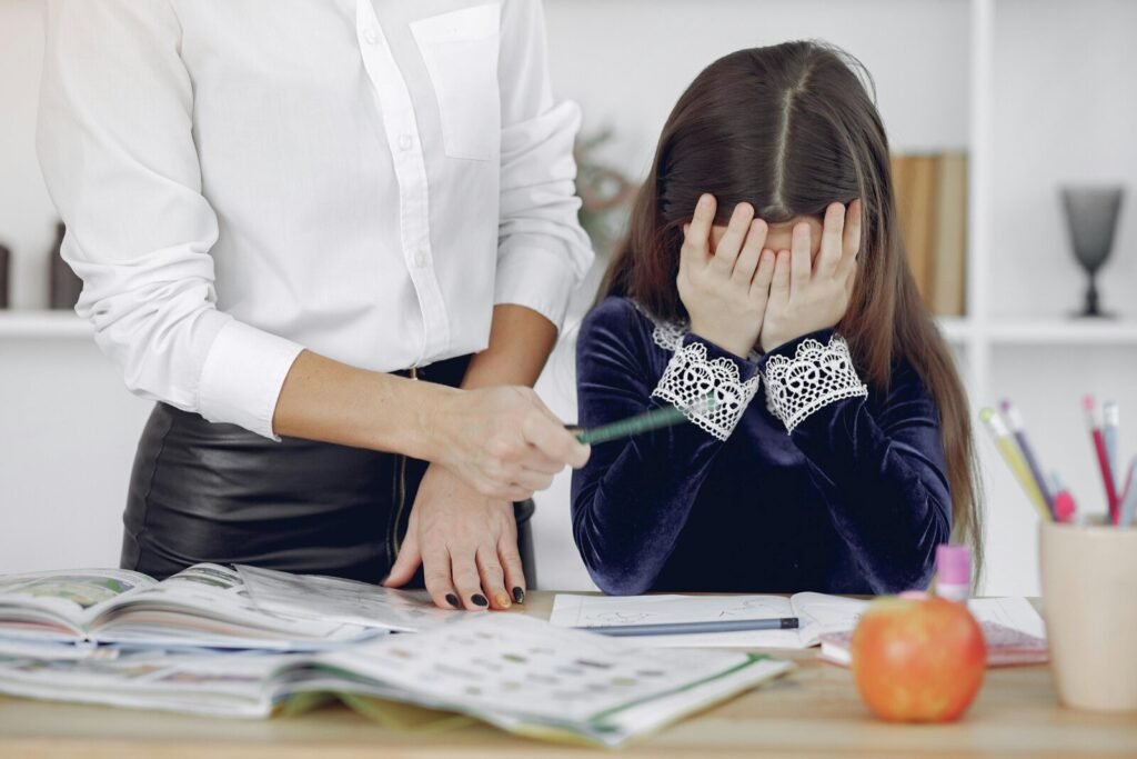 Young girl covers her face with hands while adult reaches toward papers on desk